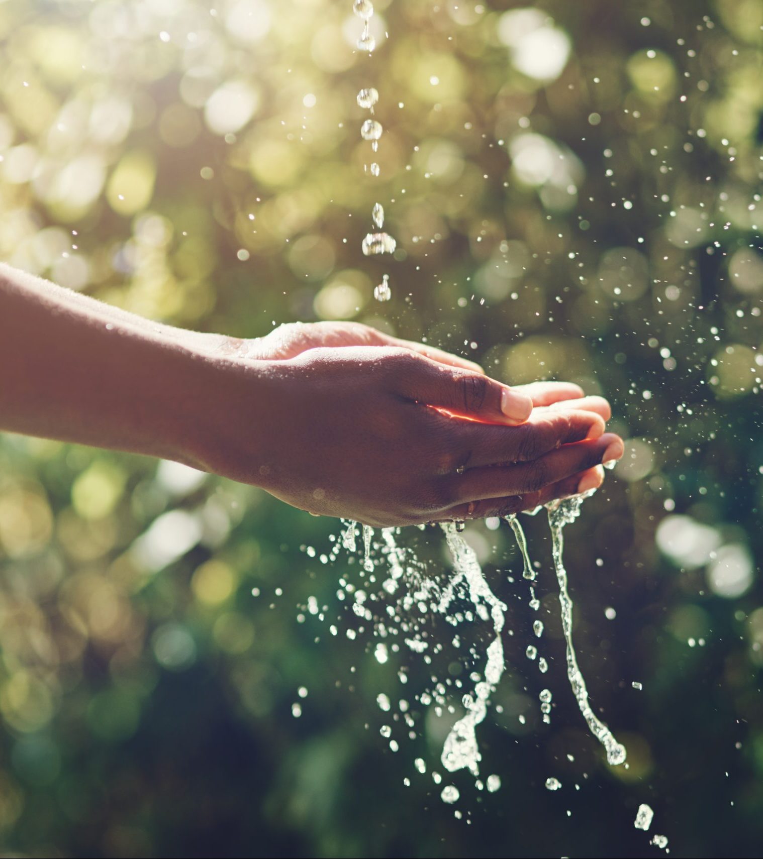 Closeup shot of a man holding his hands under a stream of water outdoors