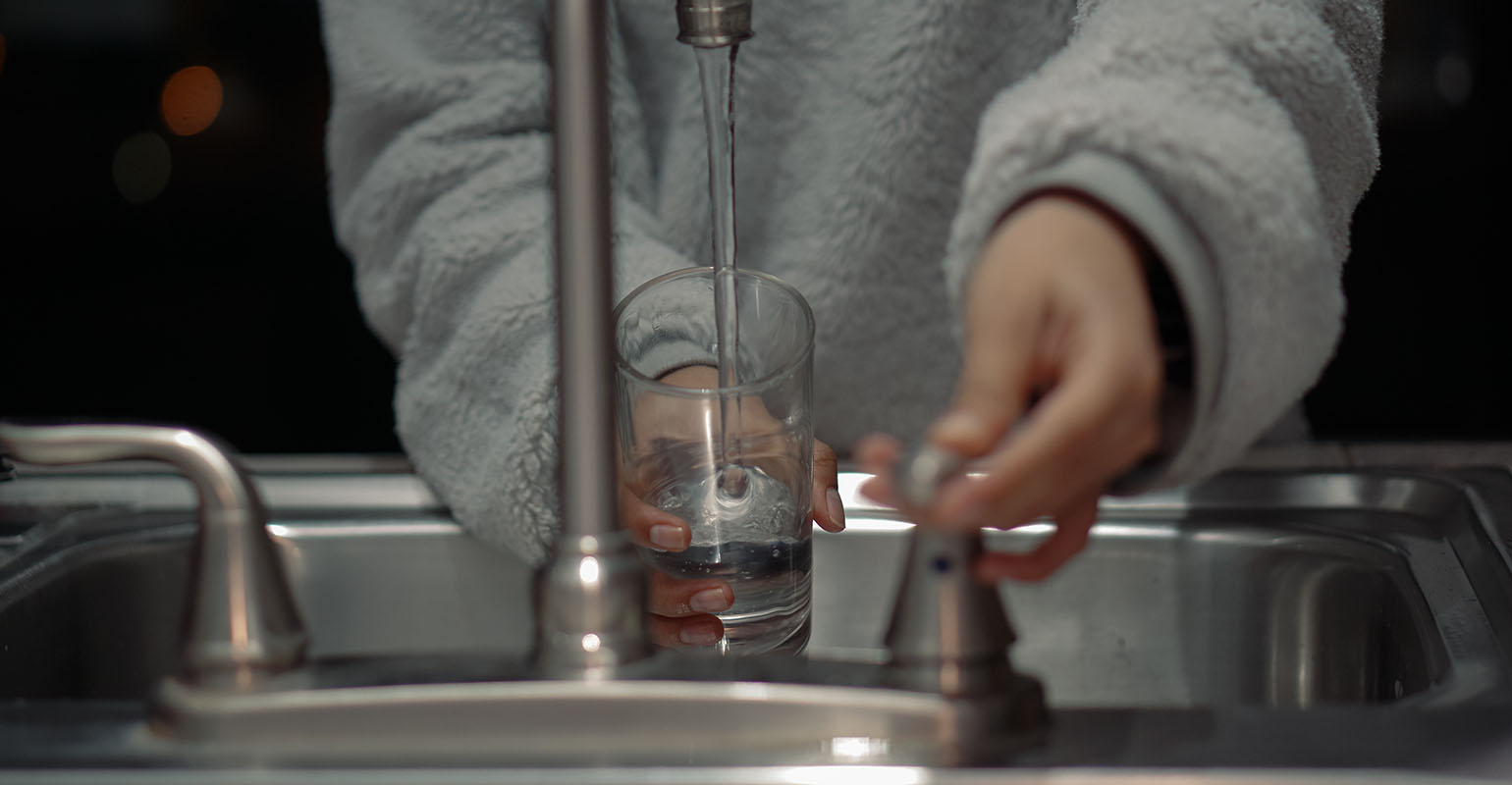 Person filling a glass with water from the tap